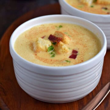 Two bowls of creamy beer and cheddar soup topped with croutons and bacon bits.