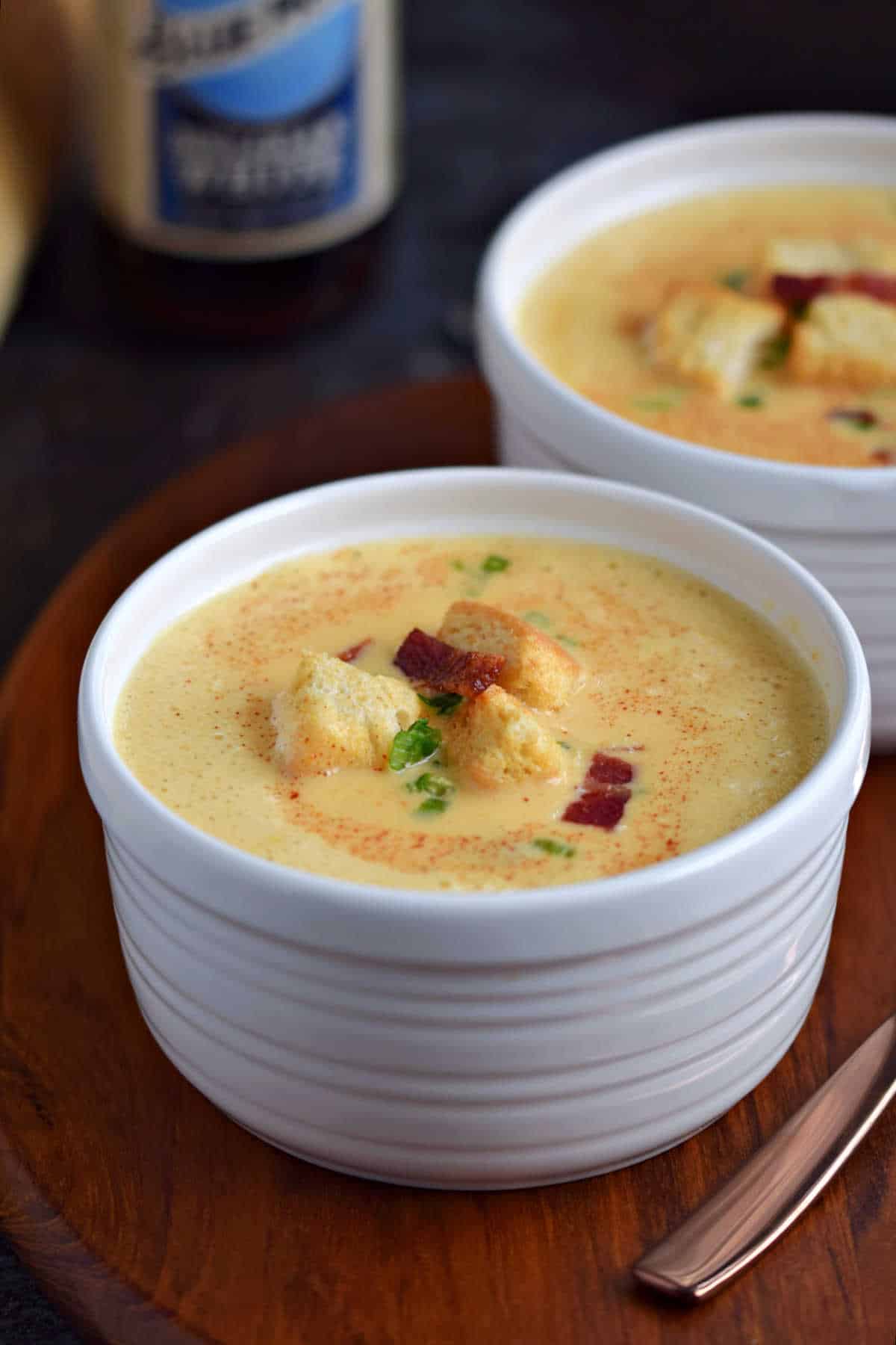 Two bowls of creamy beer and cheddar soup topped with croutons and bacon bits.