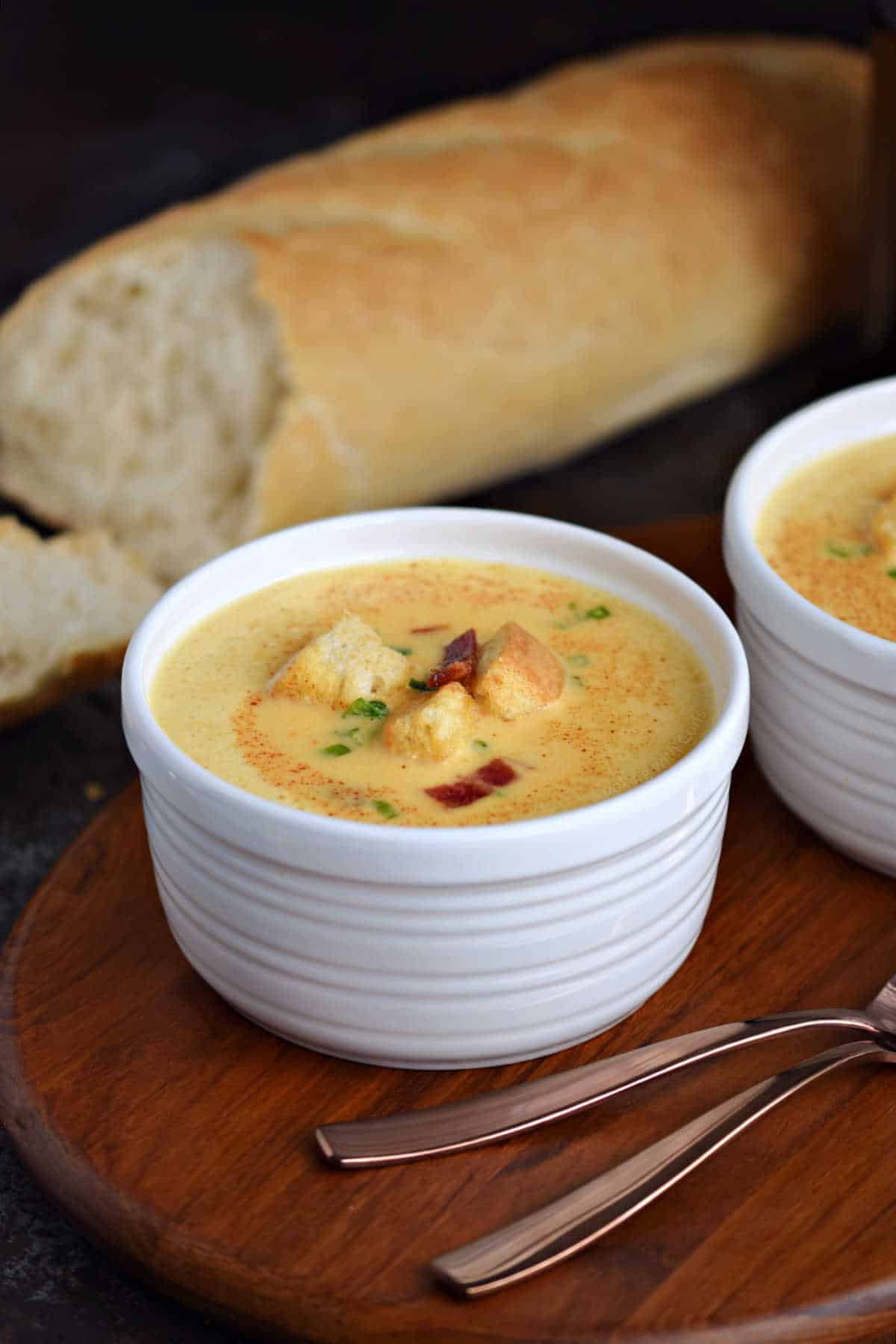 A bowl of creamy cheese soup with a loaf of crusty bread in the background.