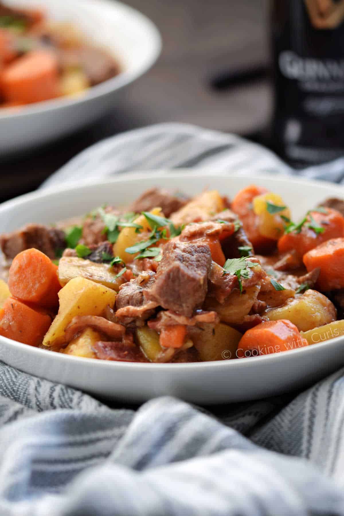 Two bowls of beef stew with carrots, potatoes and a bottle of Guinness in the background.