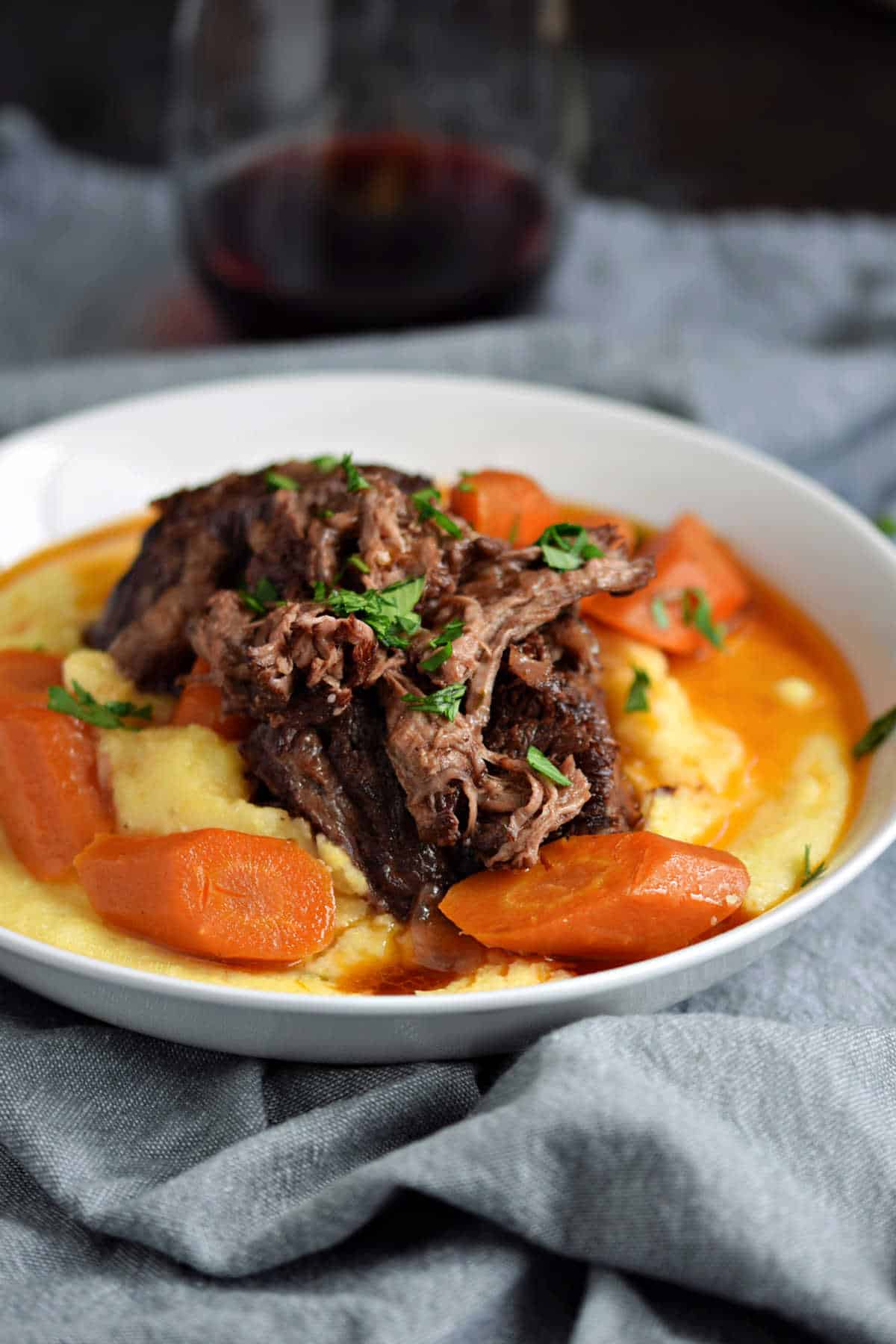 Short ribs and carrots on a bed of creamy polenta with wine gravy on top.