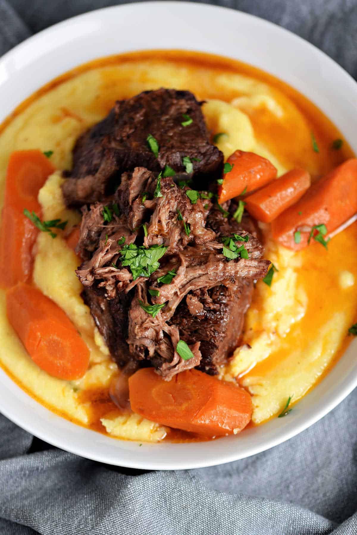 Short ribs and carrots on a bed of creamy polenta with wine gravy on top.