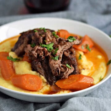 Short ribs and carrots on a bed of creamy polenta with wine gravy on top.