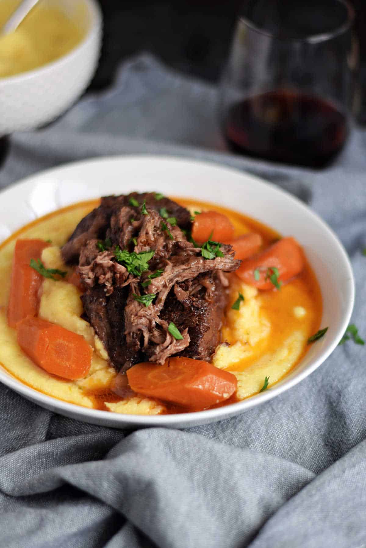 Instant Pot short ribs and carrots on a bed of creamy polenta with wine gravy on top.