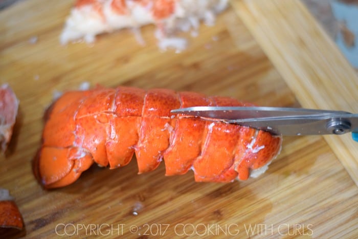 Scissors cutting through the back of the shell on the cooked lobster tail.