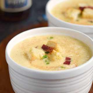 Two bowls of rich and creamy Instant Pot Cheddar-Ale Soup in white bowls garnished with croutons and bacon bits.