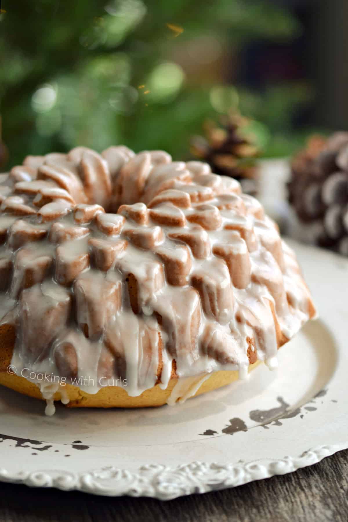 A glazed, Spiked Eggnog Bundt Cake on a serving platter sitting in front of a Christmas tree.