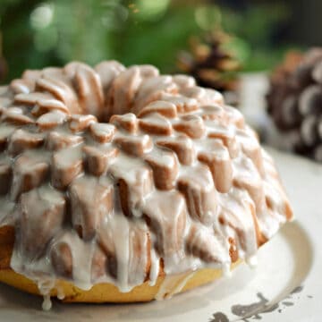 A glazed, Spiked Eggnog Bundt Cake recipe on a serving platter sitting in front of a Christmas tree.