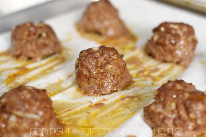 Cooked meatballs on a parchment lined baking sheet.