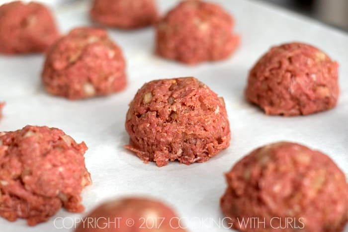 Raw meatballs on a parchment lined baking sheet.