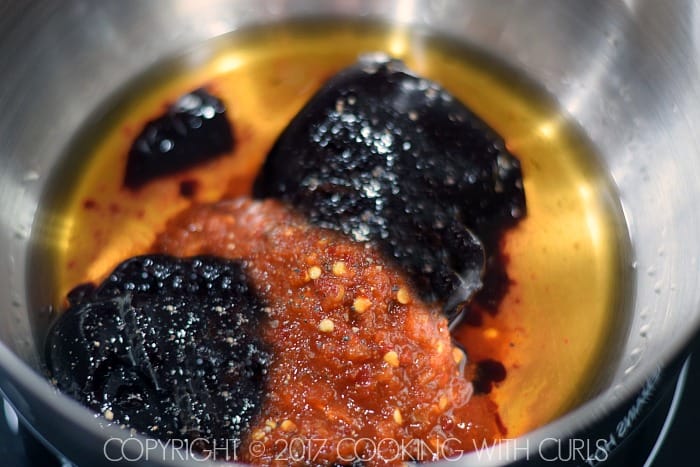 Garlic-chili paste, blackberry preserves, bourbon and black pepper in a saucepan.