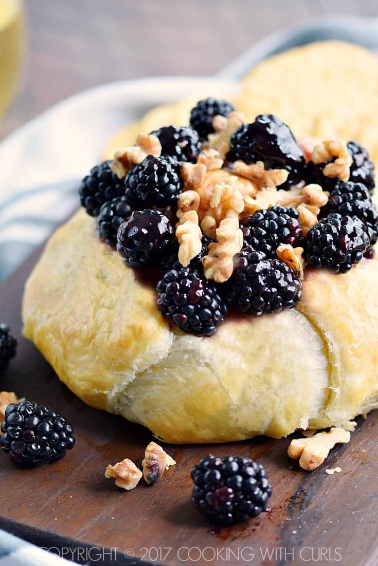 Golden brown puff pastry round topped with fresh blackberries and walnuts on a wood cutting board.