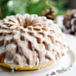 Spiked Eggnog Bundt Cake on a white platter with a tree in the background.