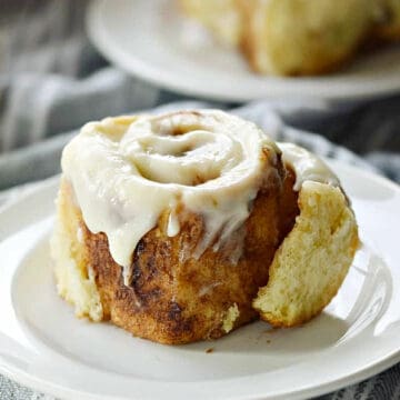 Two cinnamon rolls topped with cream cheese icing on small plates.