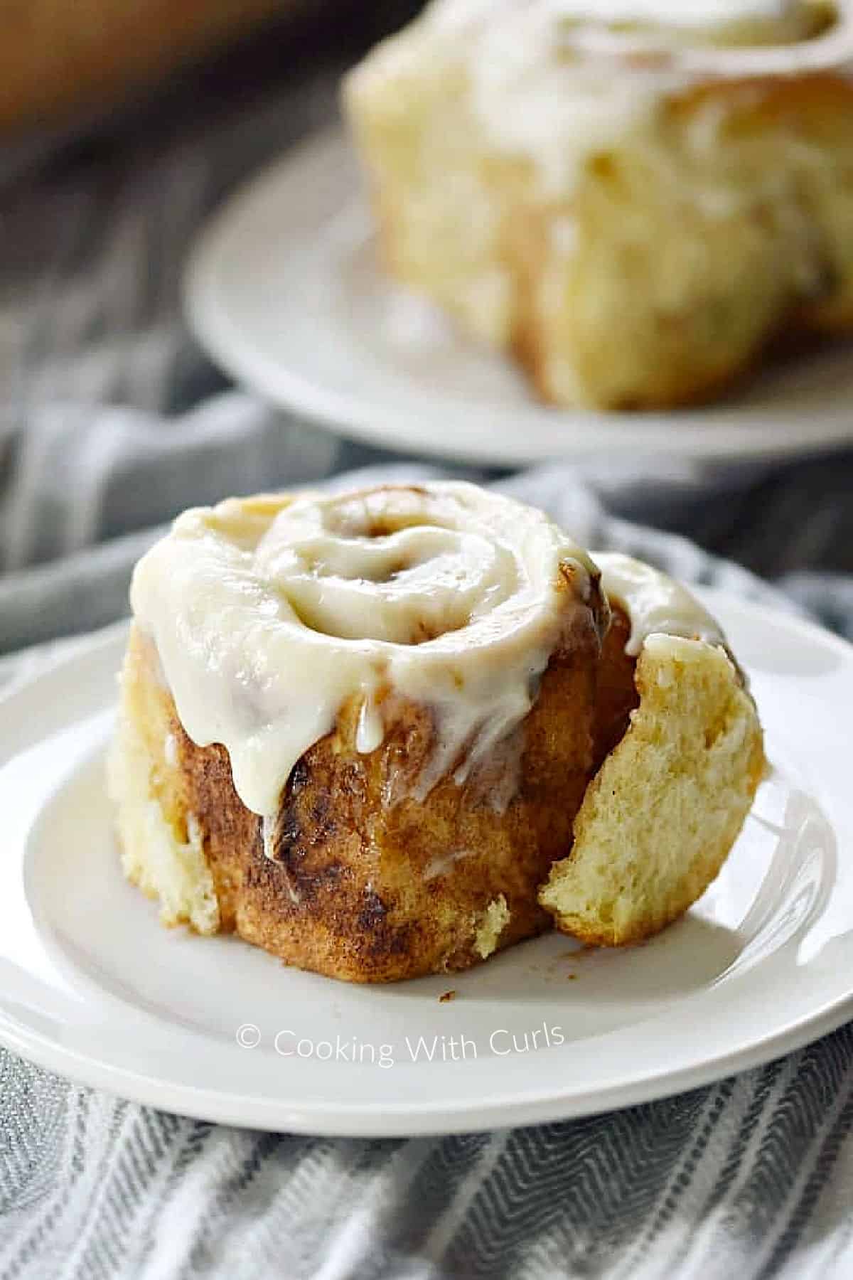 Two cinnamon rolls topped with cream cheese icing on small plates. 