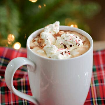 A mug of hot chocolate topped with whipped cream, chocolate sprinkles, and crushed peppermint candy.