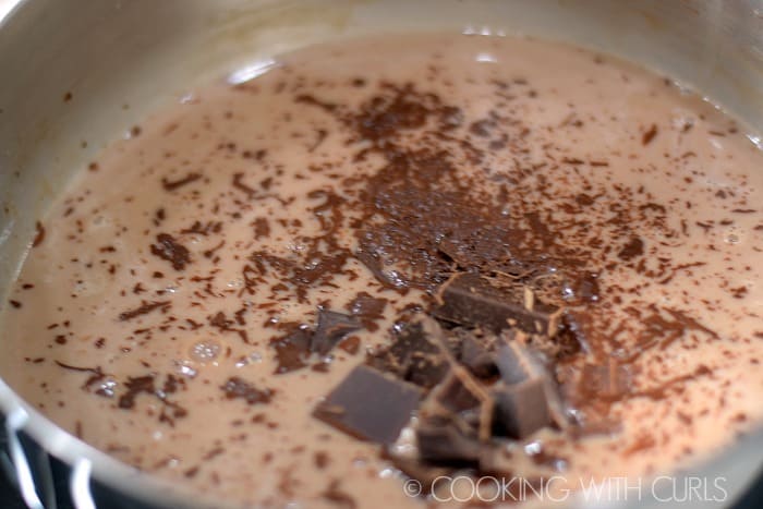 Chunks of chocolate melting into the hot milk mixture in a sauce pan.