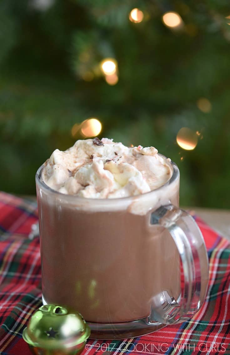 A clear mug filled with hot chocolate and topped with whipped cream.