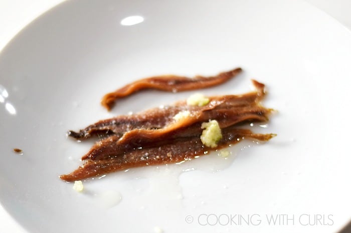 Five anchovies with pressed garlic and oil on a small plate.