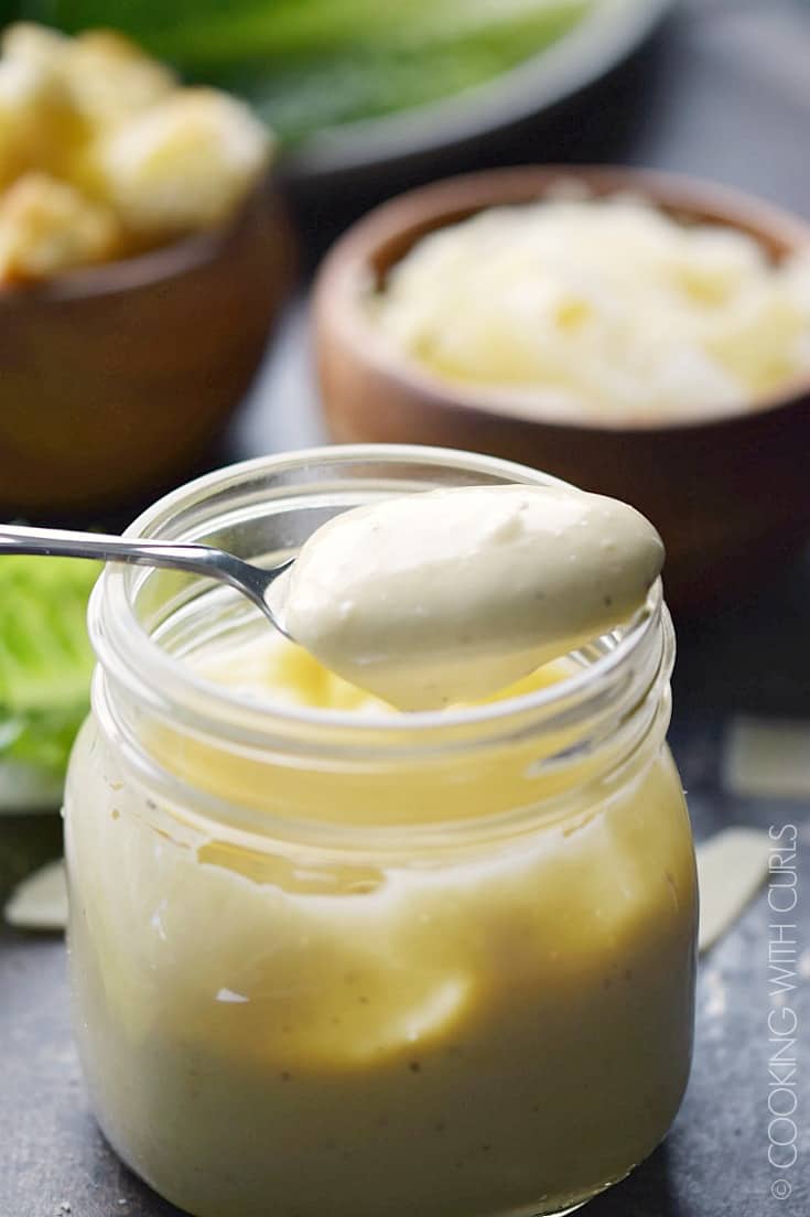 Caesar Salad Dressing in a glass jar with a spoonful of dressing sitting on top