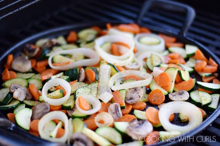 Carrots, zucchini, mushrooms, and onions cooking in a skillet on the grill