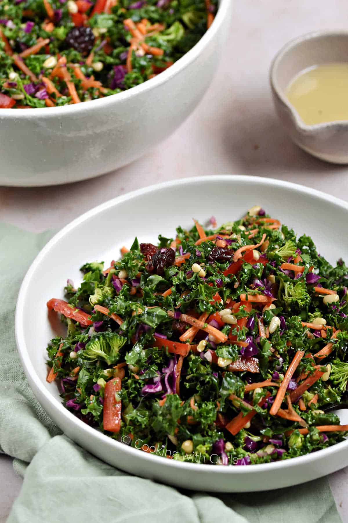 Chopped kale salad in a bowl with a container of dressing and large bowl of salad in the background.