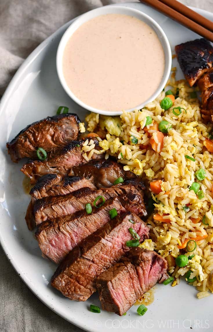 Looking down on steak and salmon with fried rice and a small bowl of Yum Yum Sauce on a large plate.