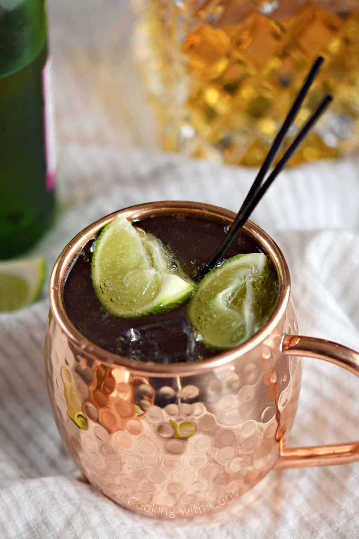 Irish Mule in a copper mug with lime wedges and bottle of whiskey and ginger beer in the background.