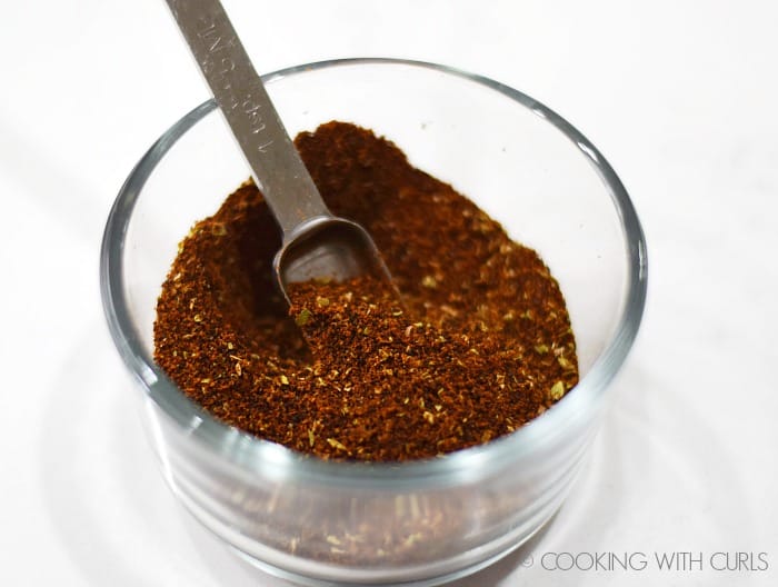 Small glass bowl with chili spice mixture and a measuring spoon
