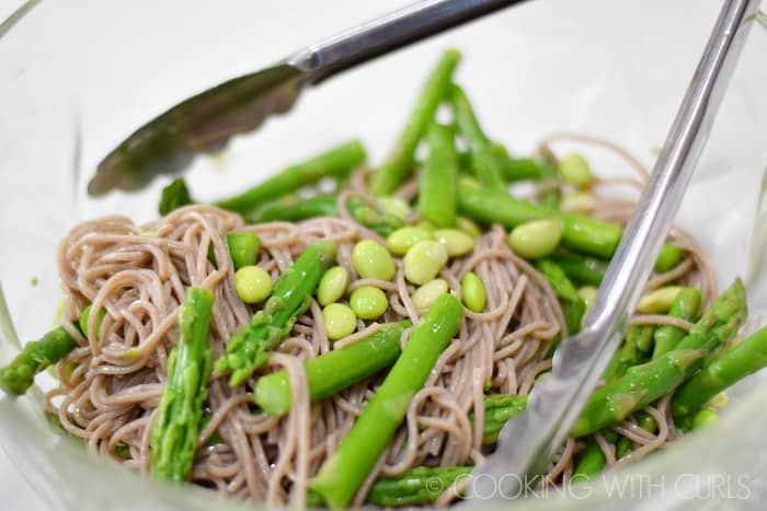 Toss the soba noodles with the asparagus and edamame in a large bowl with tongs © COOKING WITH CURLS