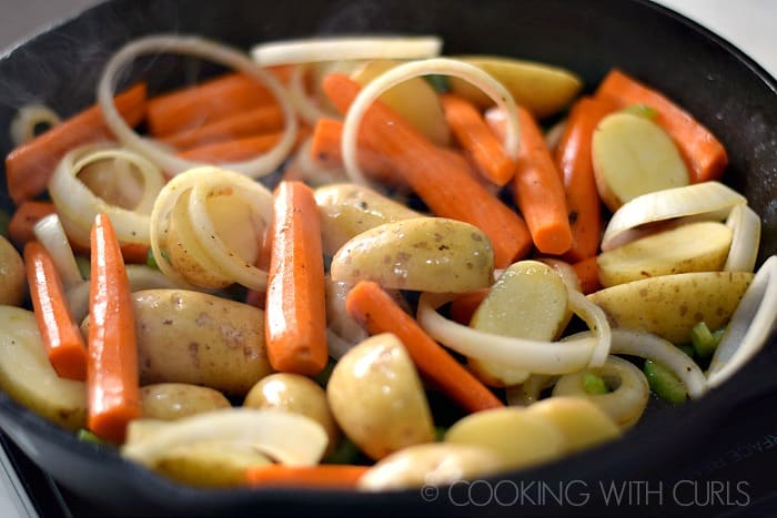 Carrots, potato halves, sliced onions, and celery slices cooking in a cast iron skillet.