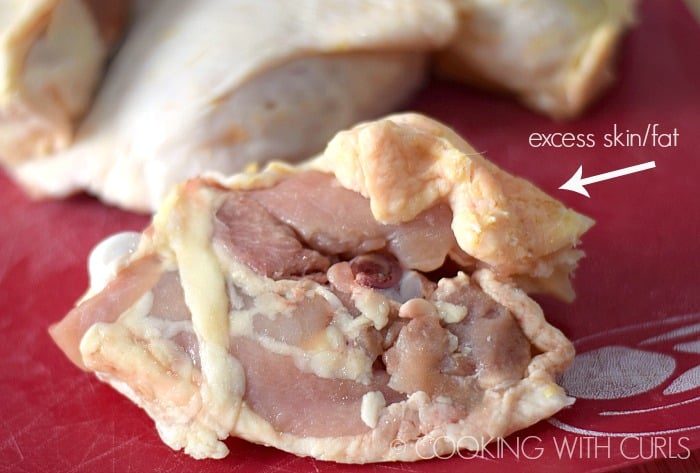 Chicken thigh sitting on a cutting board with excess skin attached.