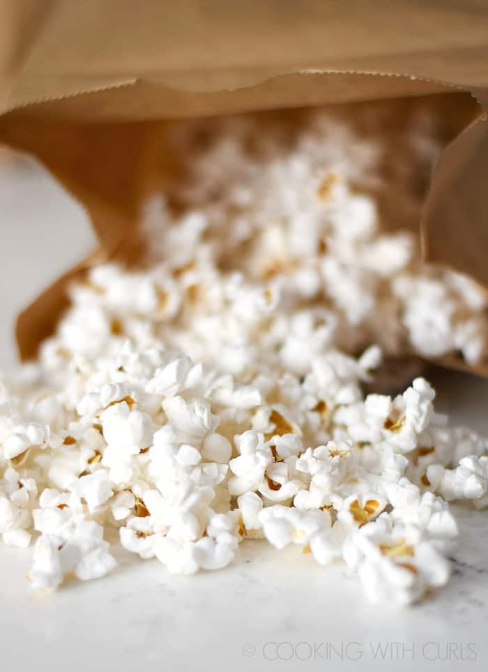 Fresh popped popcorn spilling out of a brown paper bag © COOKING WITH CURLS
