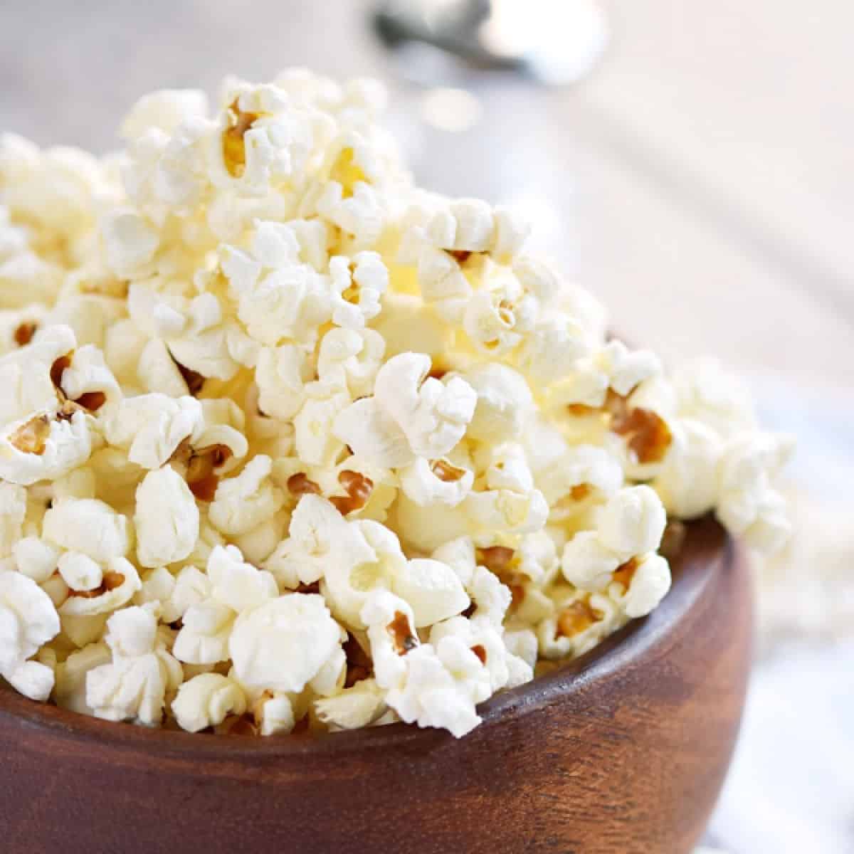 fluffy white popcorn in a wood bowl overflowing below.
