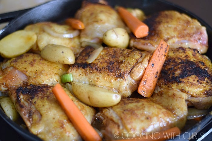 Browned chicken thighs and vegetables in a cast iron skillet.