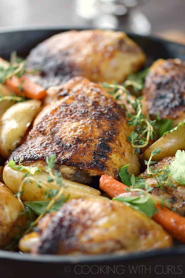 Guinness Beer-Braised Chicken Thighs with carrots, thyme sprigs, and petite potatoes in a cast iron skillet.