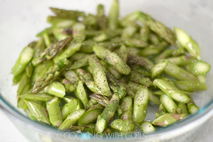 Bite size pieces of asparagus tossed in a bowl with oil, salt and pepper © COOKING WITH CURLS