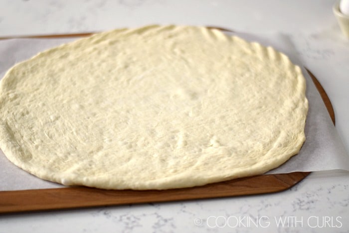 Pizza dough rolled into a circle and placed on a parchment lined pizza peel.
