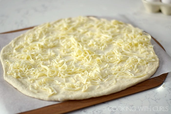 Pizza dough topped with grated Fontina cheese © COOKING WITH CURLS