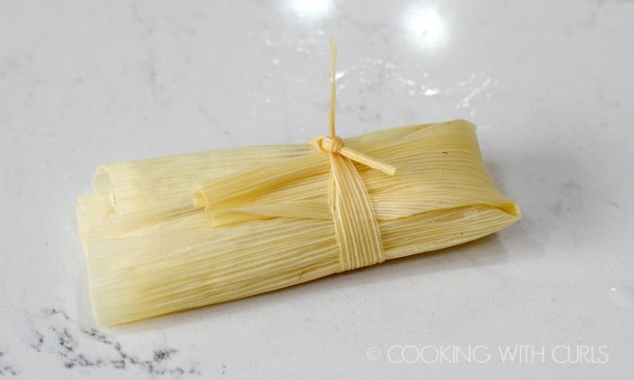 Wrap the corn husk around the masa and meat, fold up the end and tie with a thin strip of husk to hold it together © COOKING WITH CURLS