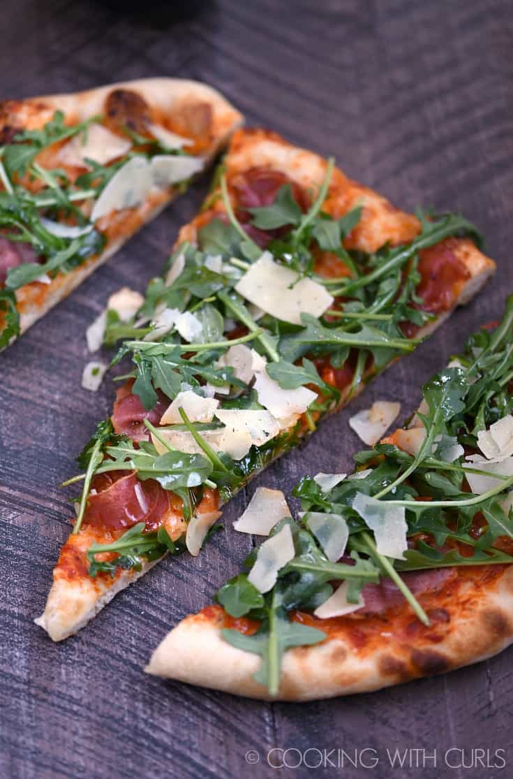 Three slices of pizza topped with prosciutto, arugula, shaved parmesan cheese, and tomato sauce.
