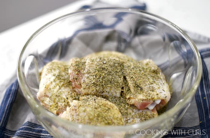 Chicken thighs coated in seasoning in a large glass bowl © COOKING WITH CURLS
