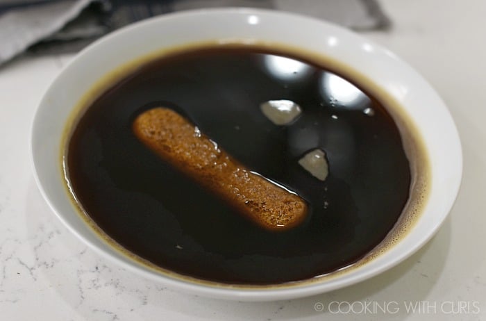 Ladyfinger dipped in a small bowl of coffee mixture.