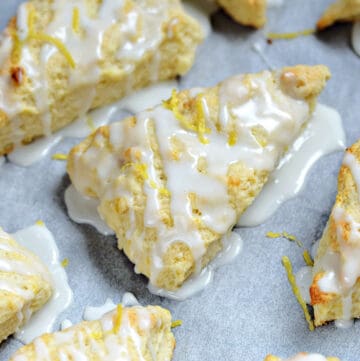 Lemon Scones recipe drizzled with glaze randomly places on parchment paper and sprinkled with lemon zest.