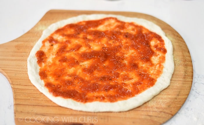 Pizza dough on a wooden pizza peel topped with tomato sauce.