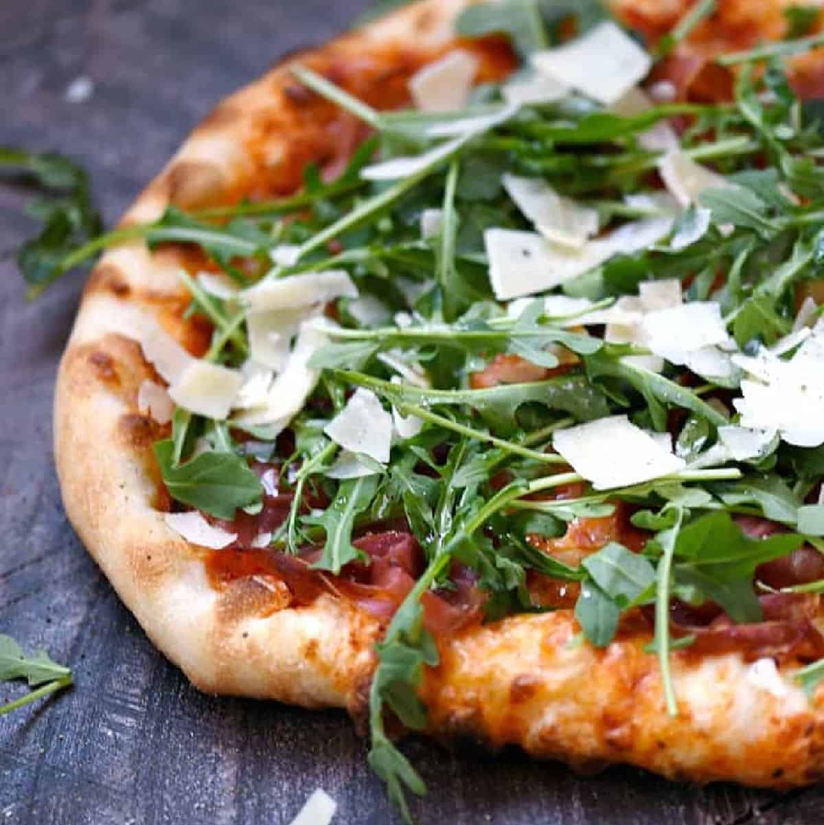 Pizza topped with prosciutto slices, arugula, and shaved parmesan cheese.