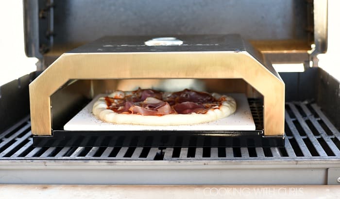 Pizza inside a pizza oven on a gas grill.