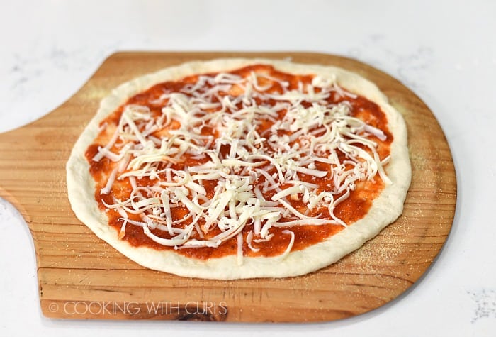 Sprinkle grated mozzarella cheese over the pizza sauce.
