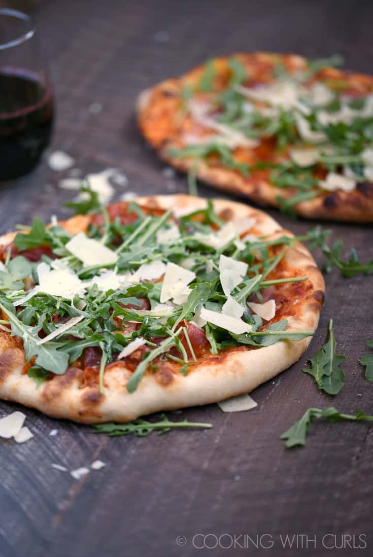 Two pizzas topped with prosciutto, arugula, shaved parmesan cheese, and tomato sauce.