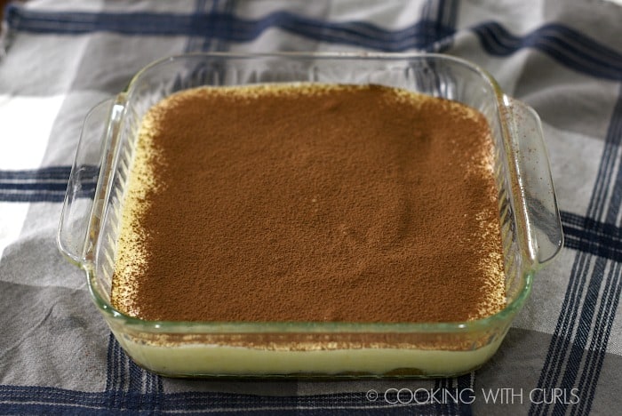 The first layer of ladyfingers and mascarpone cream sprinkled with cocoa in a baking dish.